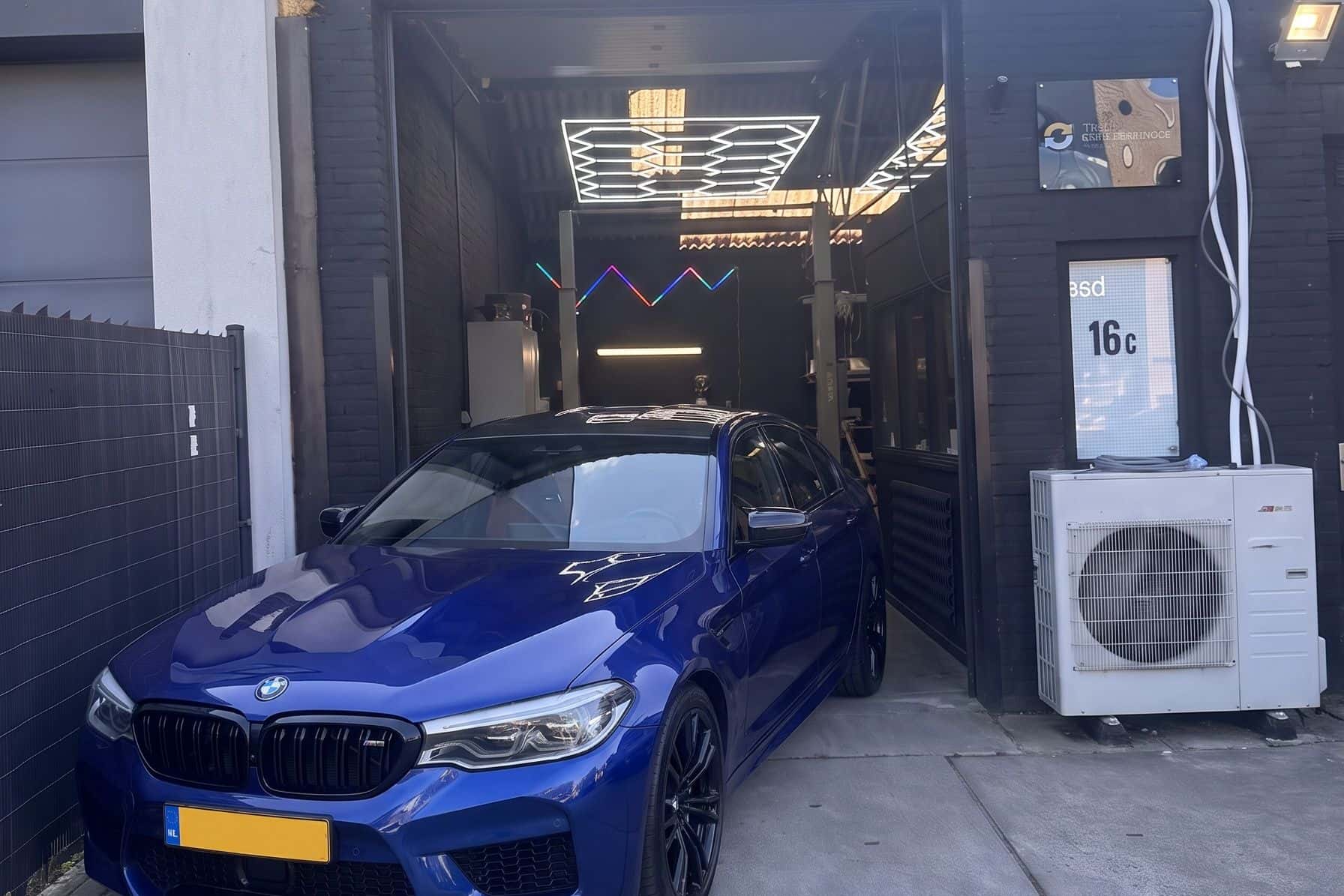 Blauwe BMW M5 voor de geopende roldeur van de werkplaats