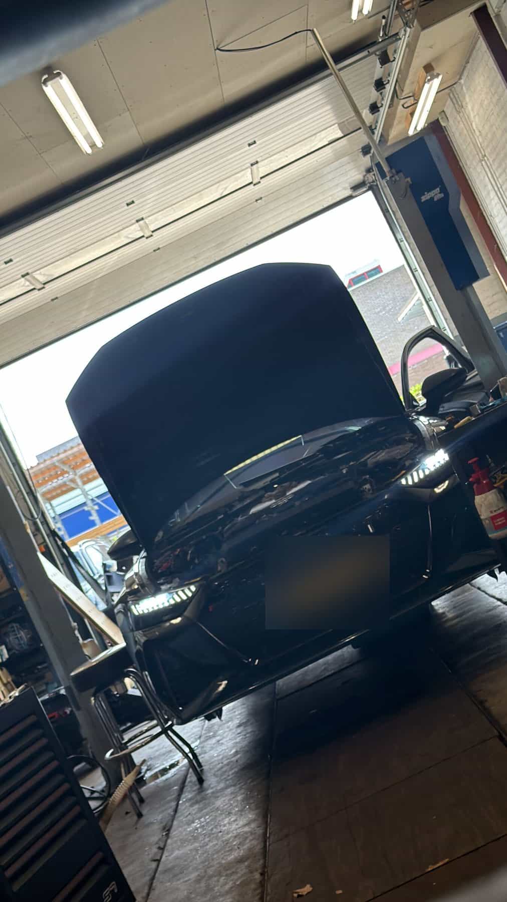 Auto met geopende motorkap op de brug bij de roldeur
