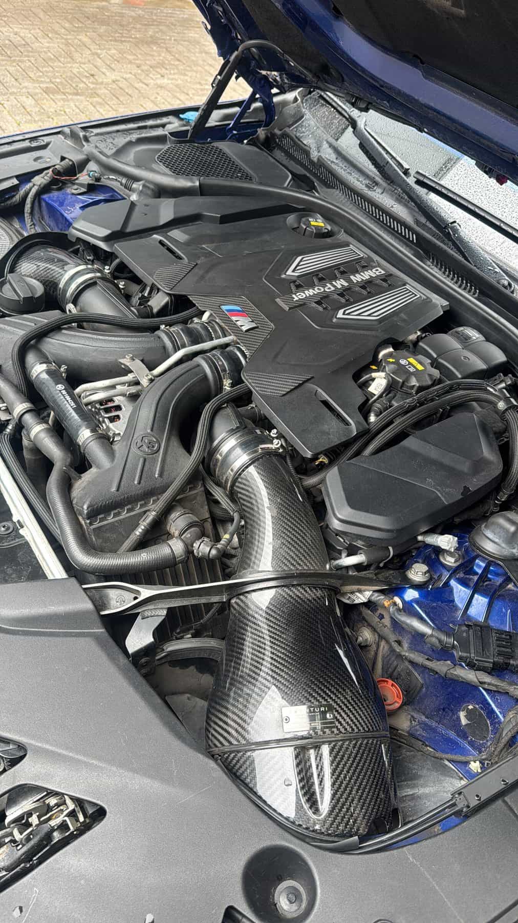 Geopende motorruimte van een sportieve auto met carbon luchtinlaat